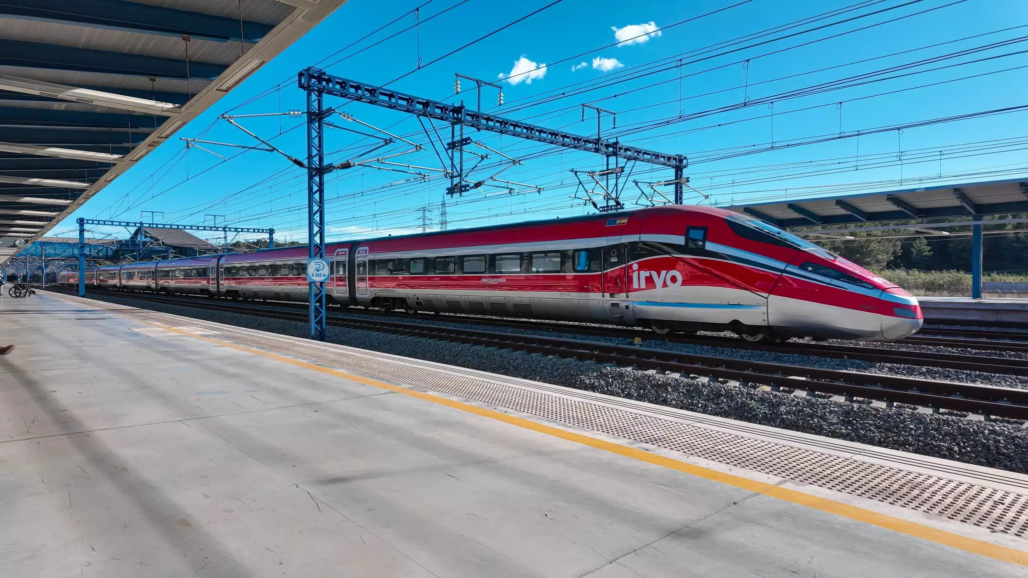 A high-speed red train running on tracks through a station.