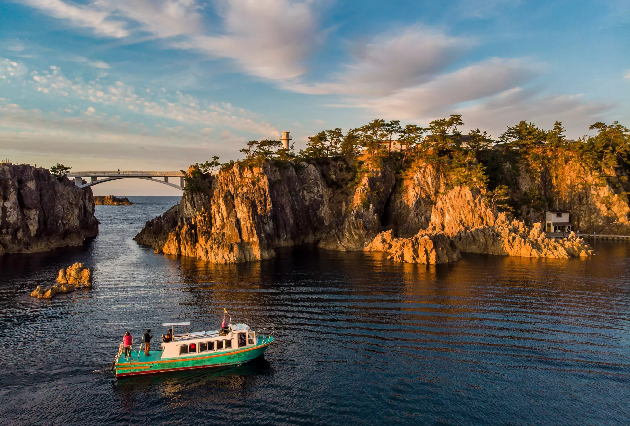 A small boat with passengers cruises through a bay as sunset casts an orange glow on the rocky coastline.