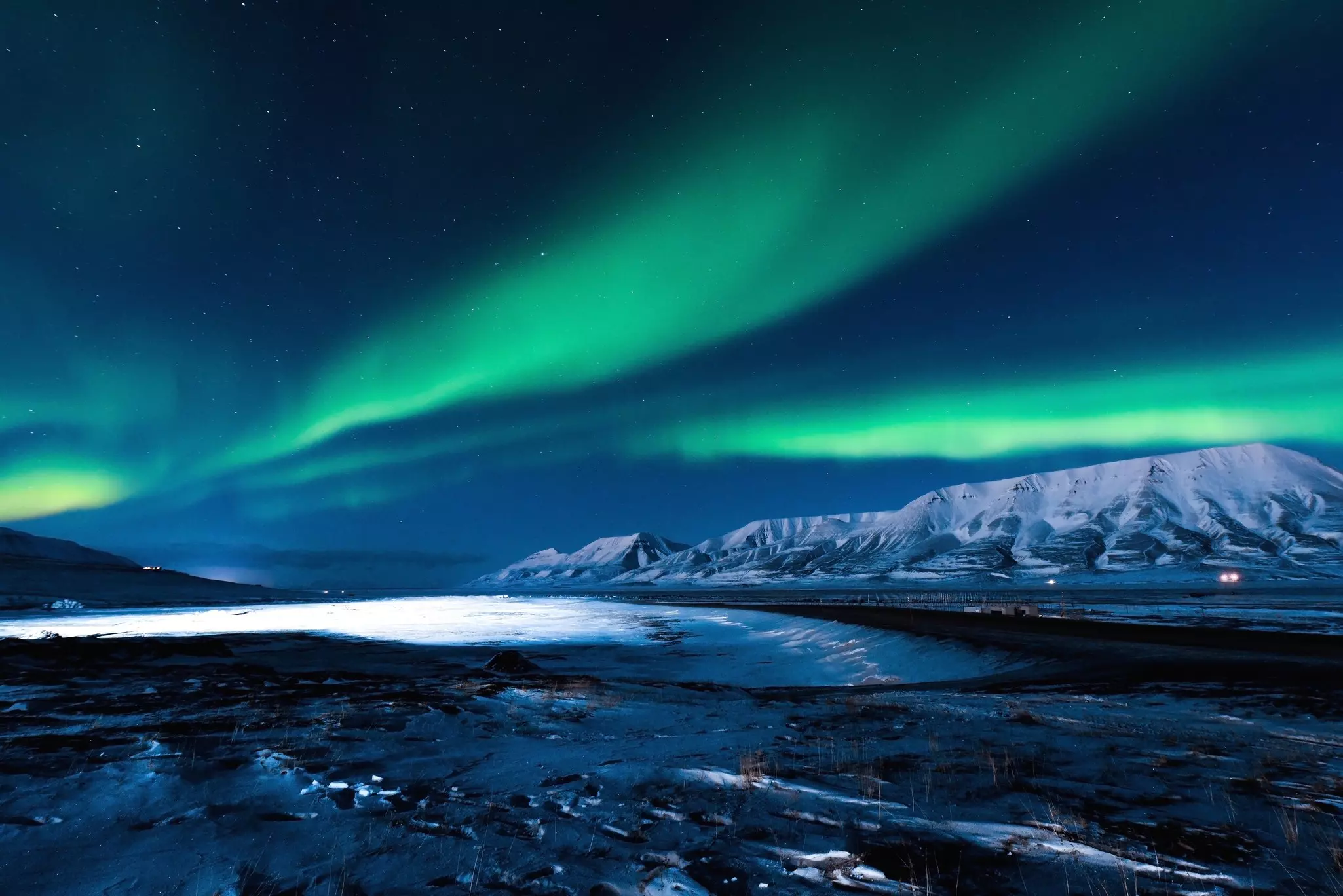 The bright green and rich blue northern lights in Svalbard, Norway over ice-topped mountains and ground