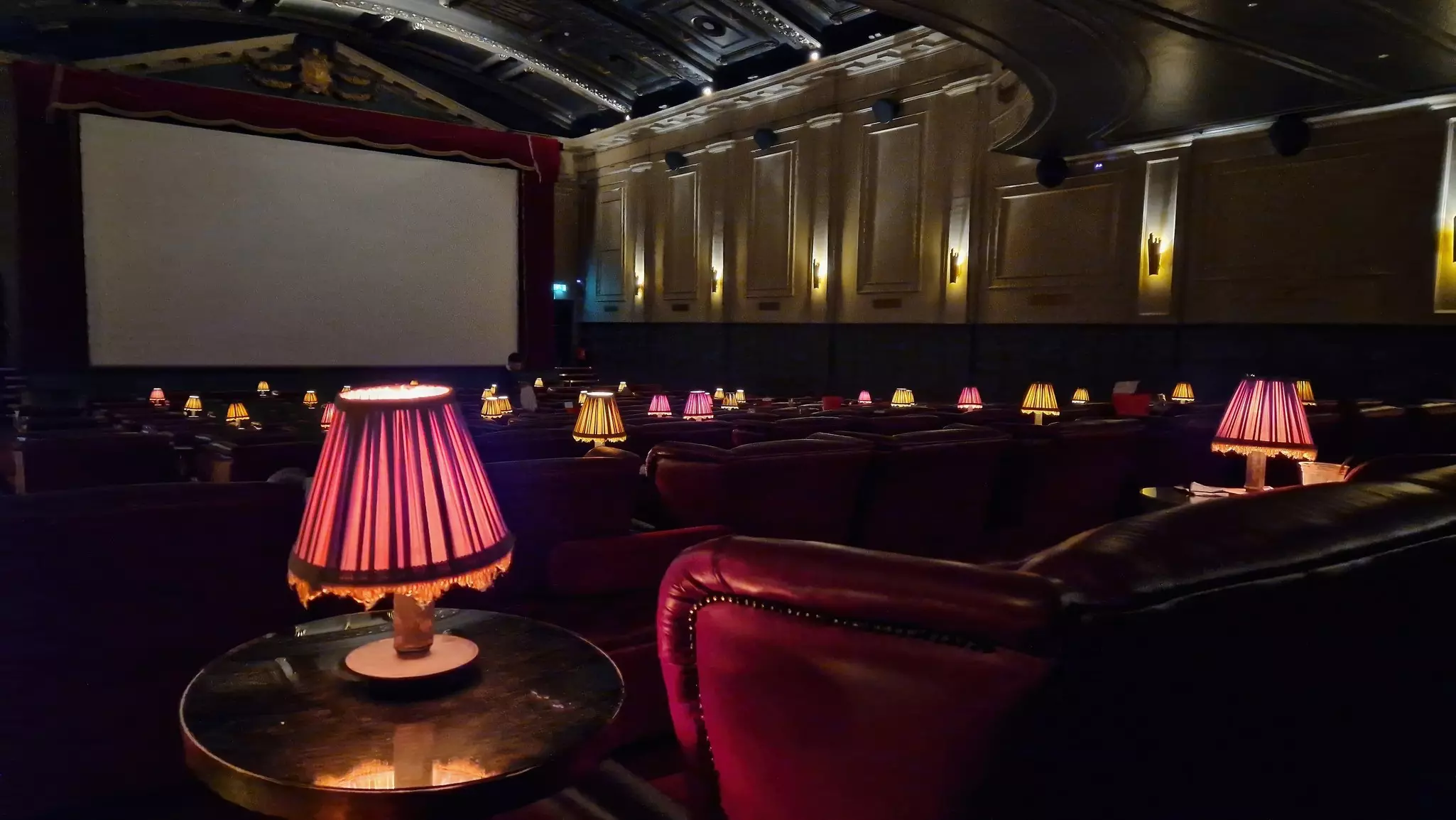 Interior of a retro cinema with leather couches and low light coming from freestanding lamps on tables