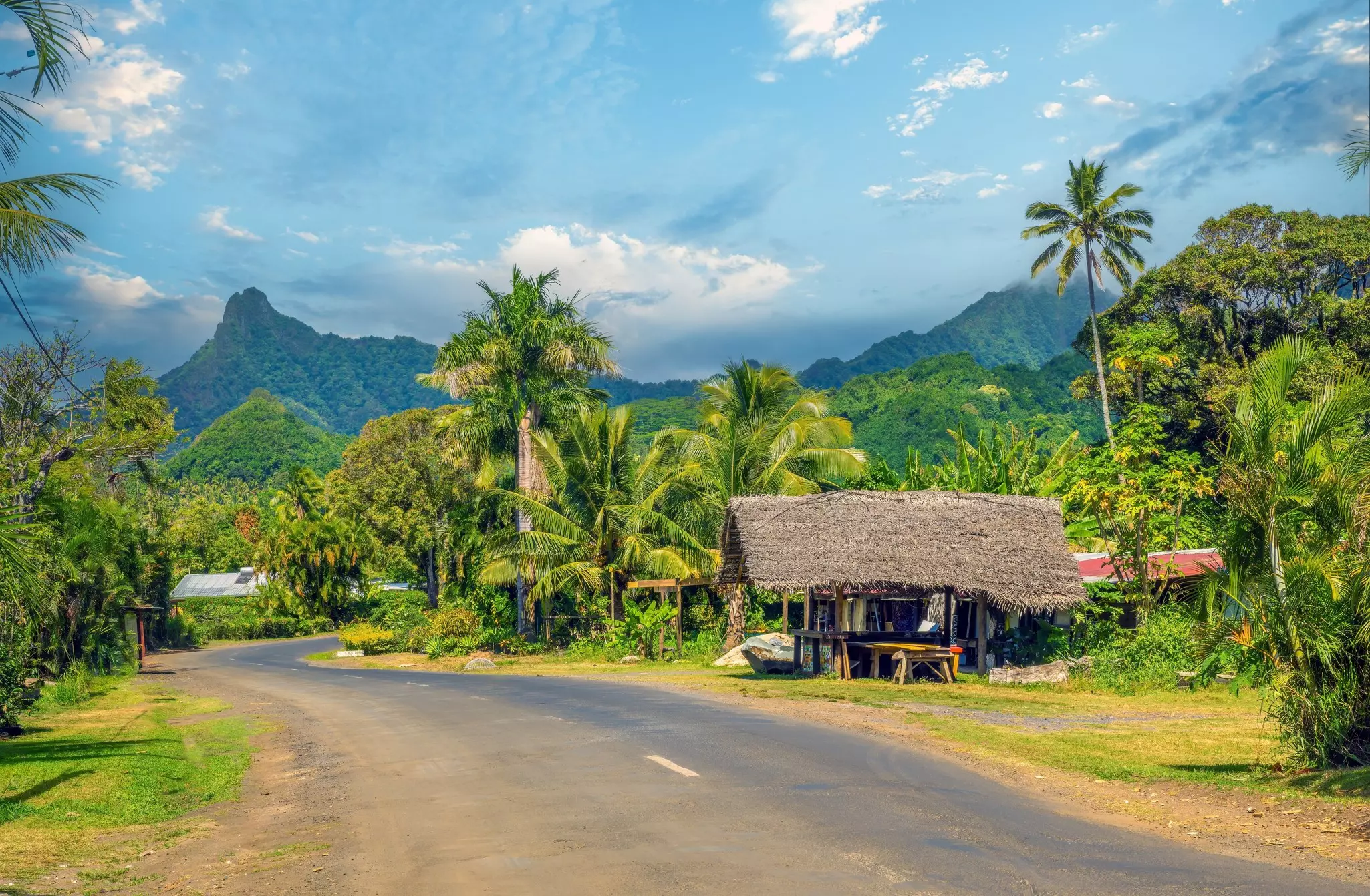 A winding road through a hilly tropical landscape with a wooden shelter beside the road. 