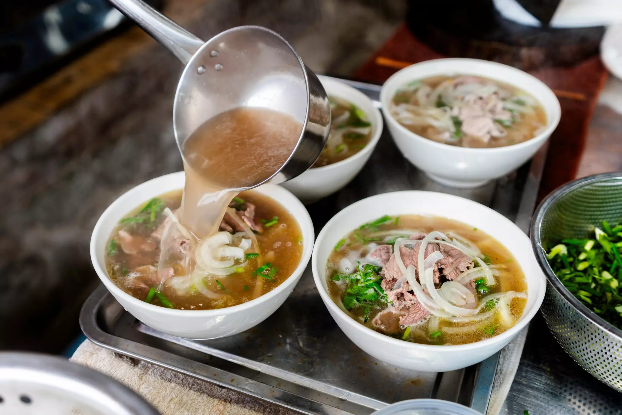Four bowls of pho topped with scallions and onions and beef.