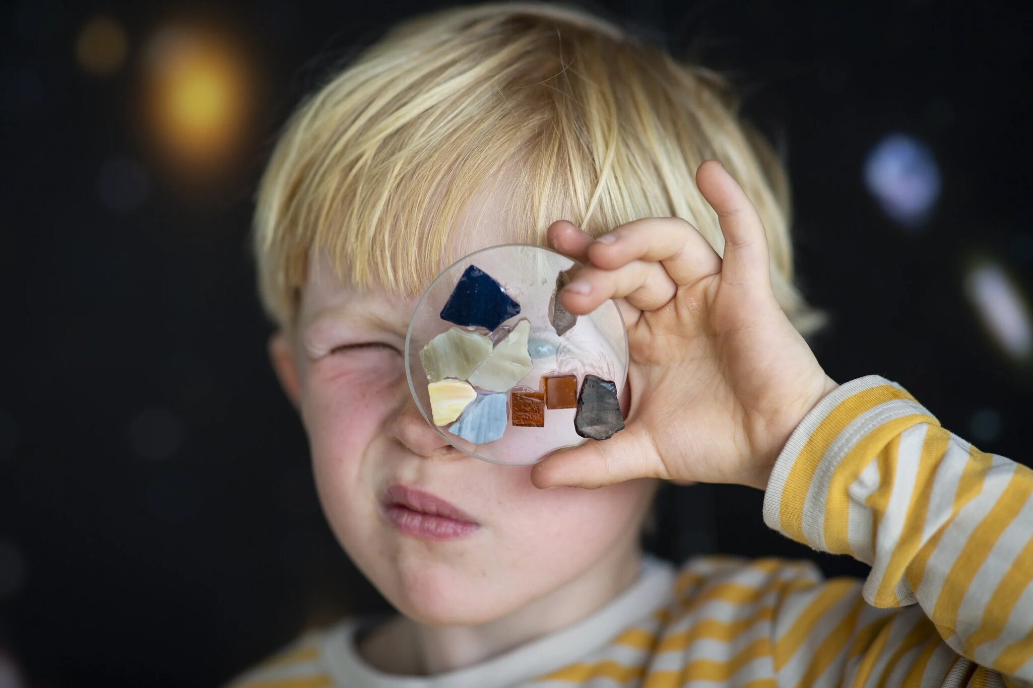 A young boy holding a circular glass design over his eye in Glasmuseet Ebeltoft in Ebeltoft, Jutland, Denmark. 