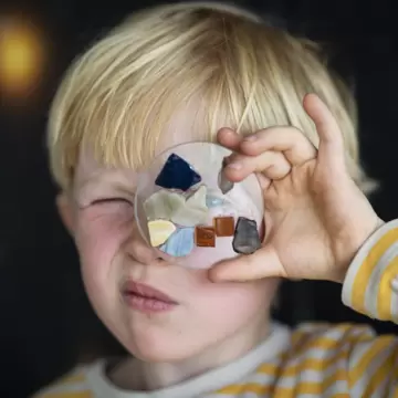 A young boy holding a circular glass design over his eye in Glasmuseet Ebeltoft in Ebeltoft, Jutland, Denmark. 