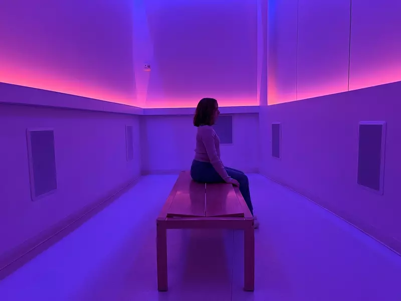 A person sitting on a bench in a room filled with purple and magenta light.