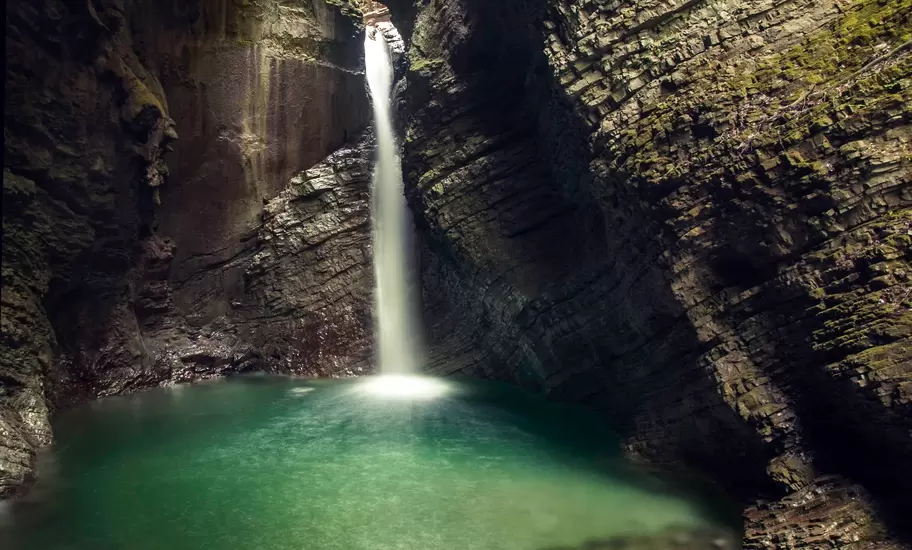 Kozjak waterfall near Kobarid, Slovenia, dropping through a narrow rock cleft into a green pool inside a mossy cavern