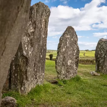 Close up of Drombeg Stone Circle with green grass and blue sky.
