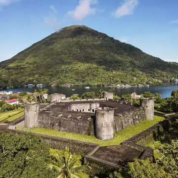 A large star-shaped fortress on a lush island near a volcano