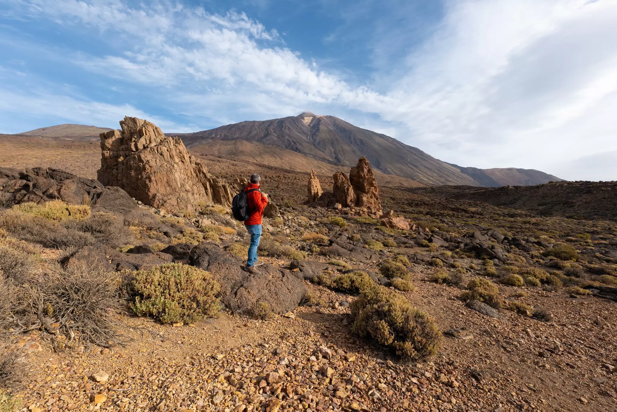 A hiker stands on a volcanic hiking trail looking towards a high mountain peak, Mt Teide in Tenerife, Spain