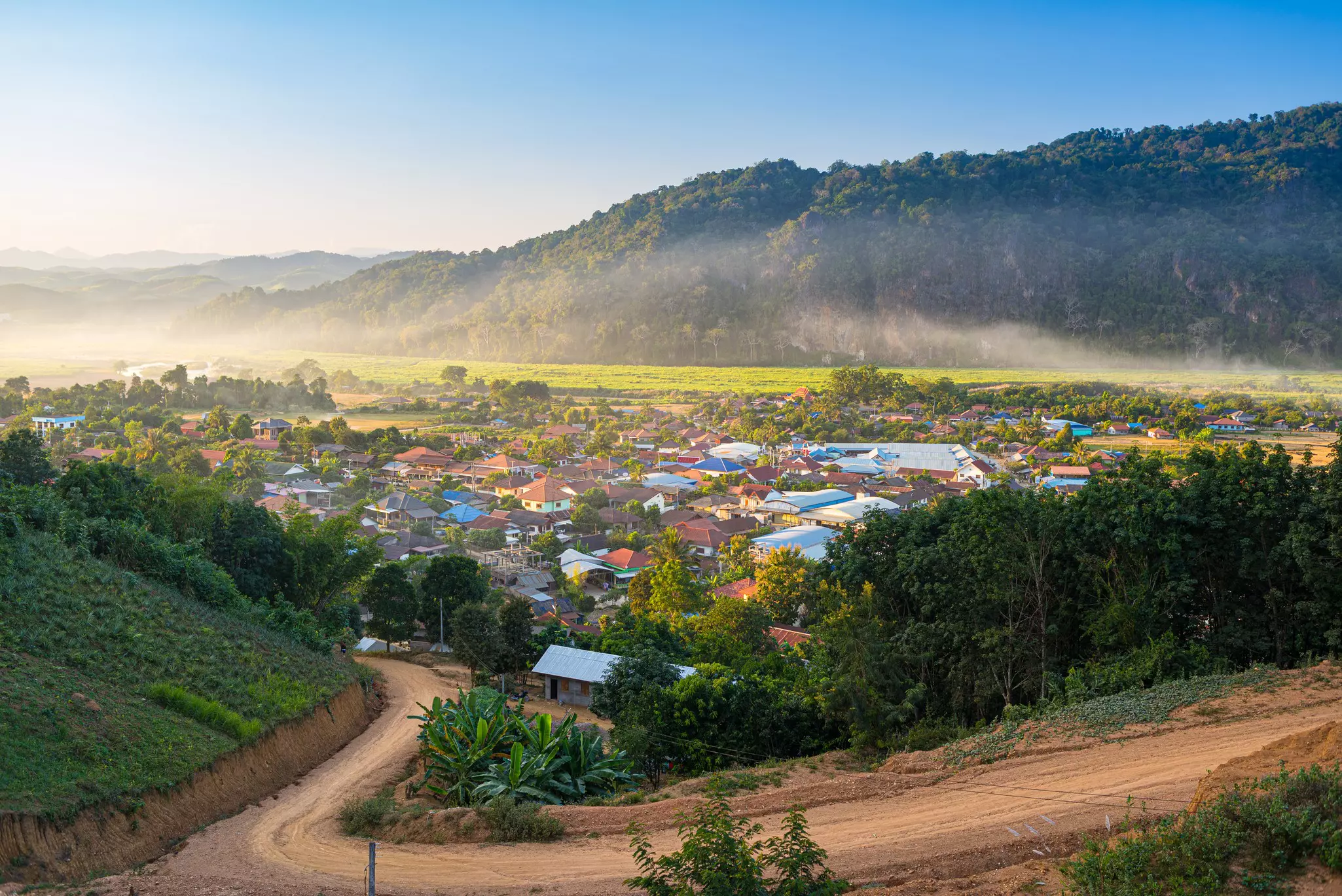 Mountain mist above crops near a small village.