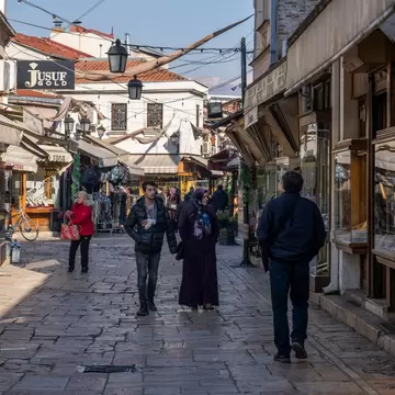 Stone-paved street lined with jewellery shop windows and canvas awnings, a few people walking in sunlight.