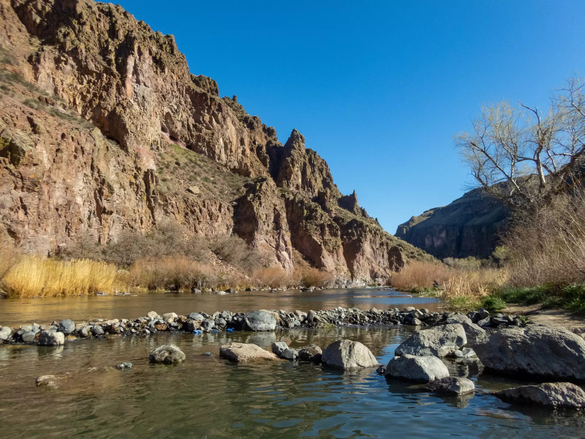 A river bordered by a low red rock mountain on a sunny day.