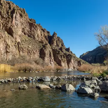 A river bordered by a low red rock mountain on a sunny day.