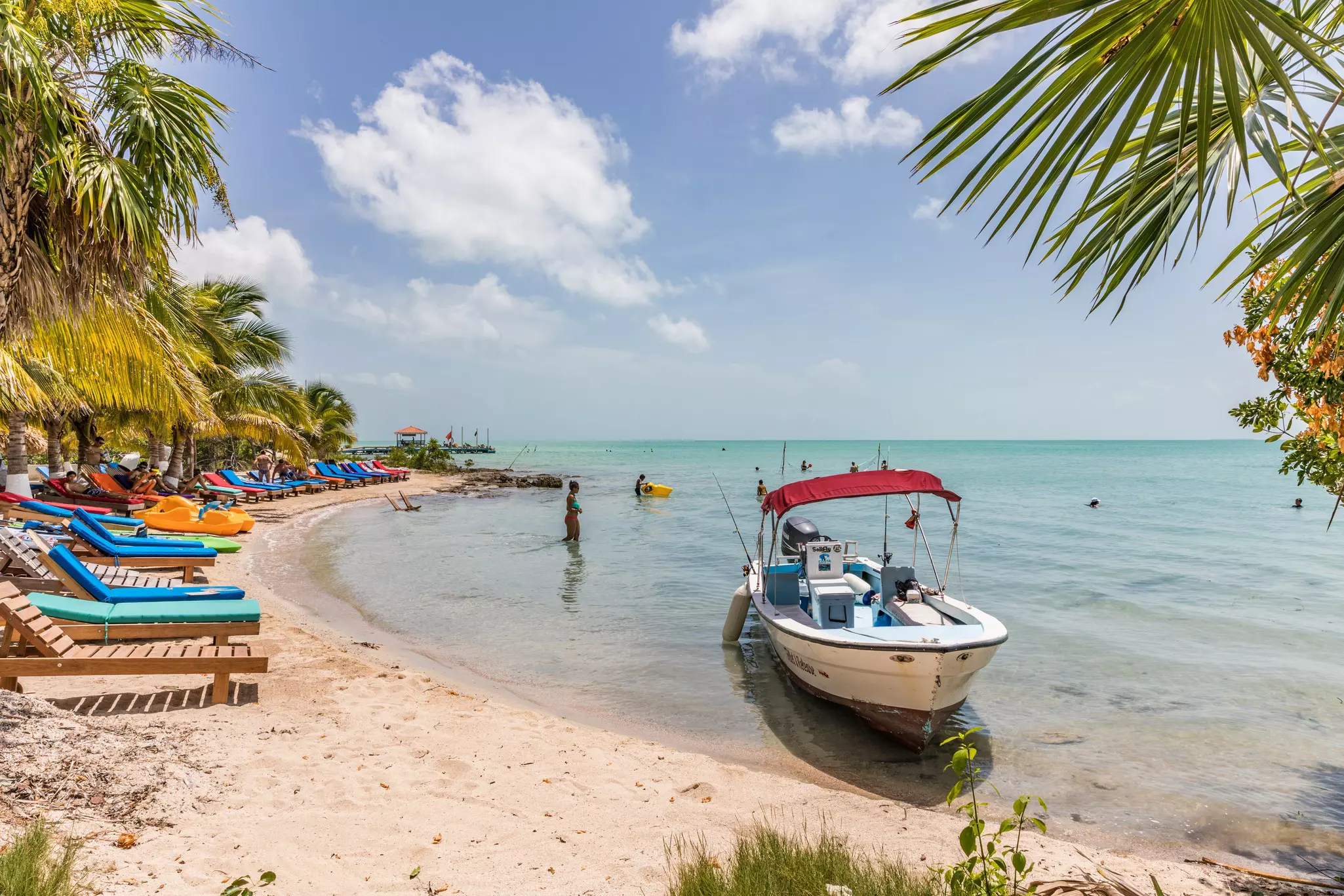 Sunloungers line a small beach cove with a boat anchored nearby in the shallows