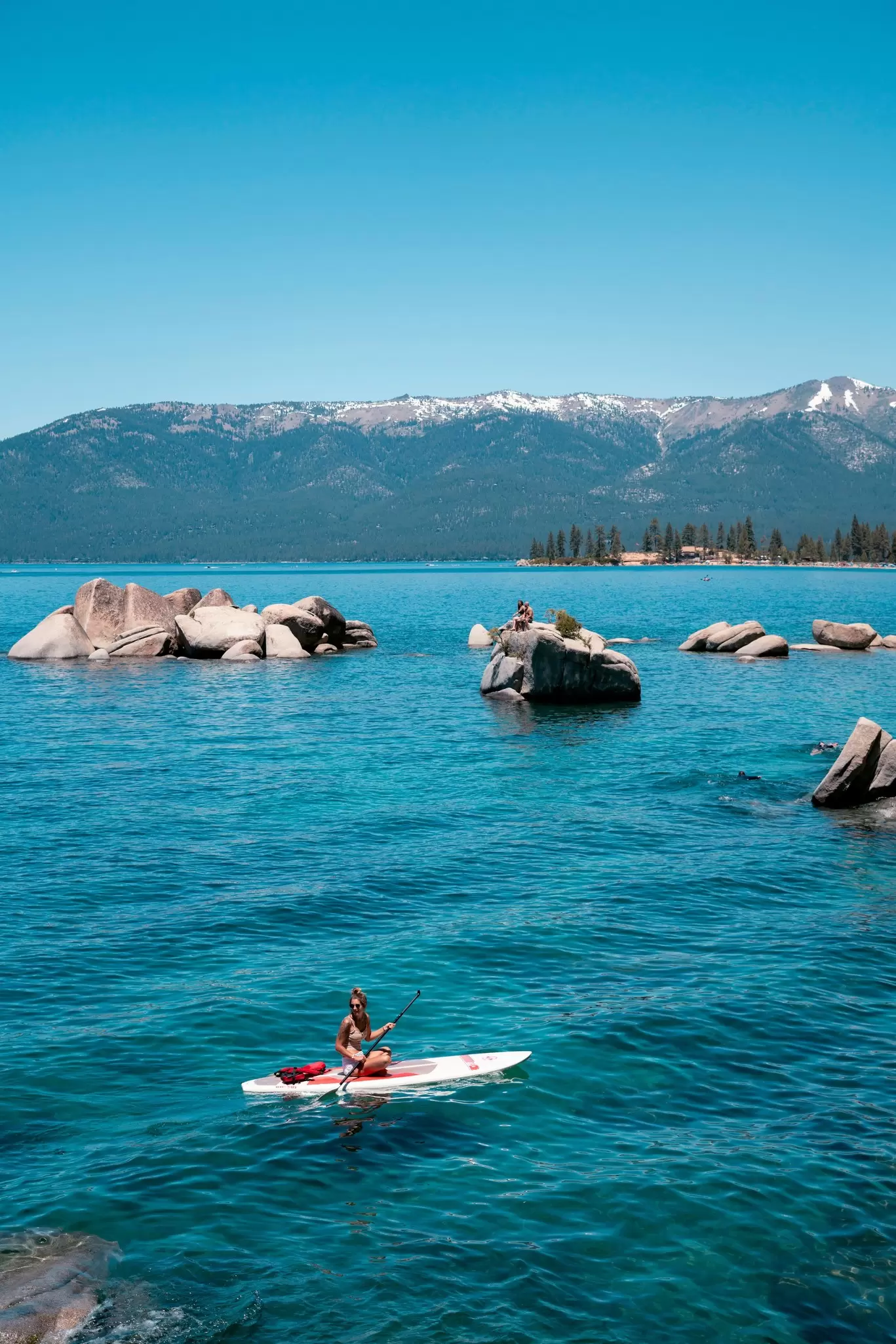 A person sitting on a paddleboard in a blue lake with large rocks. 