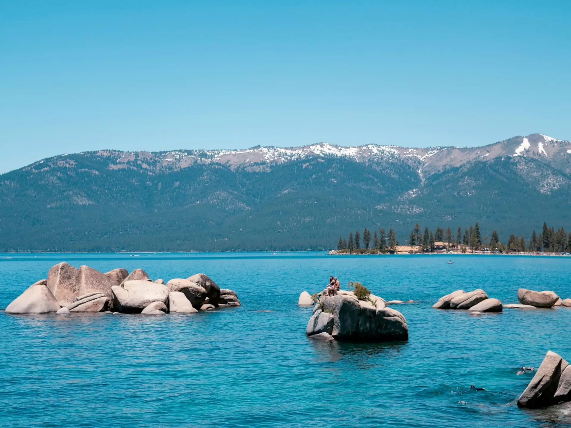 A person sitting on a paddleboard in a blue lake with large rocks. 