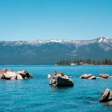 A person sitting on a paddleboard in a blue lake with large rocks. 