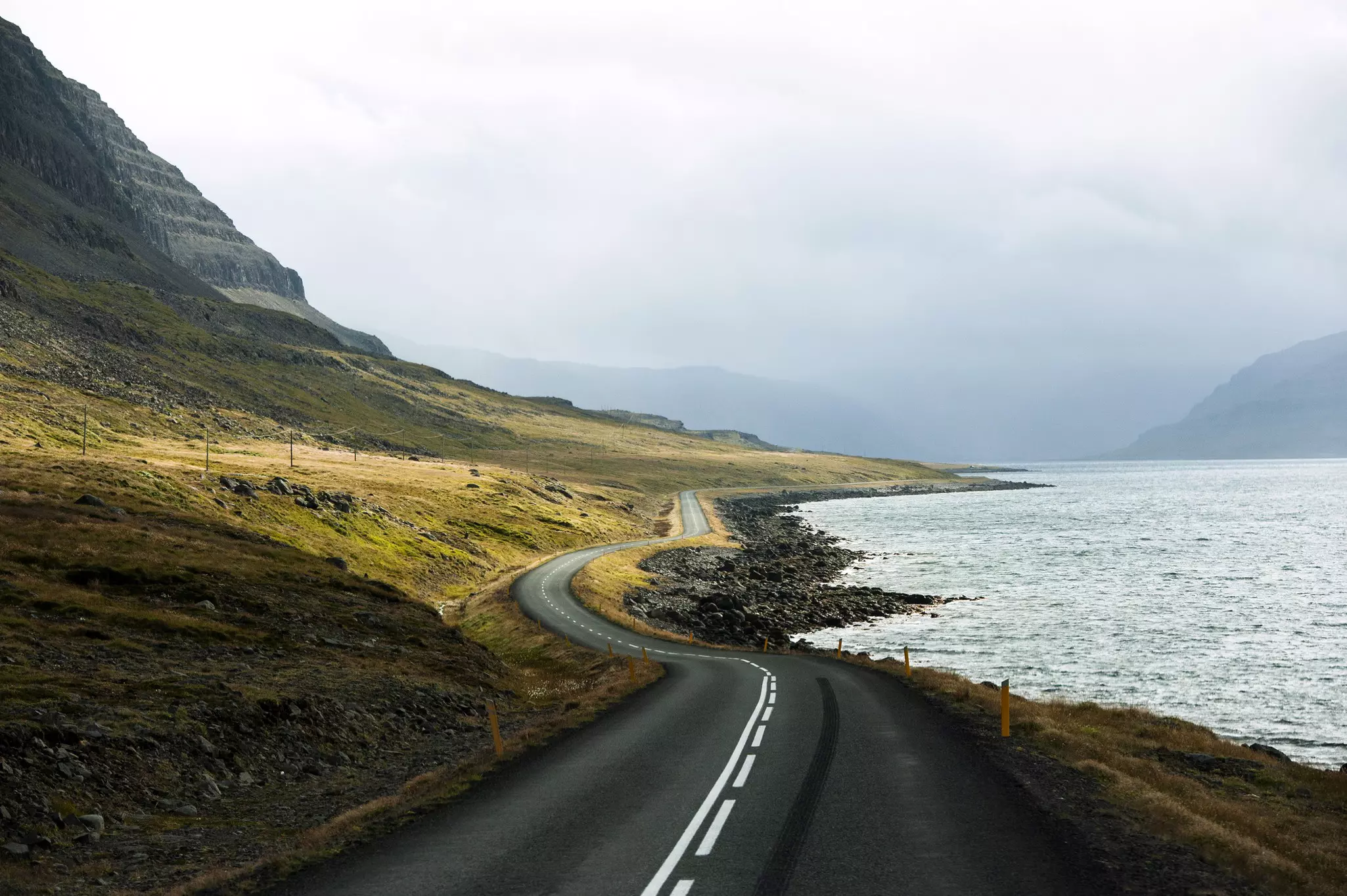 A road winding along a rocky coast, with mountains to the left