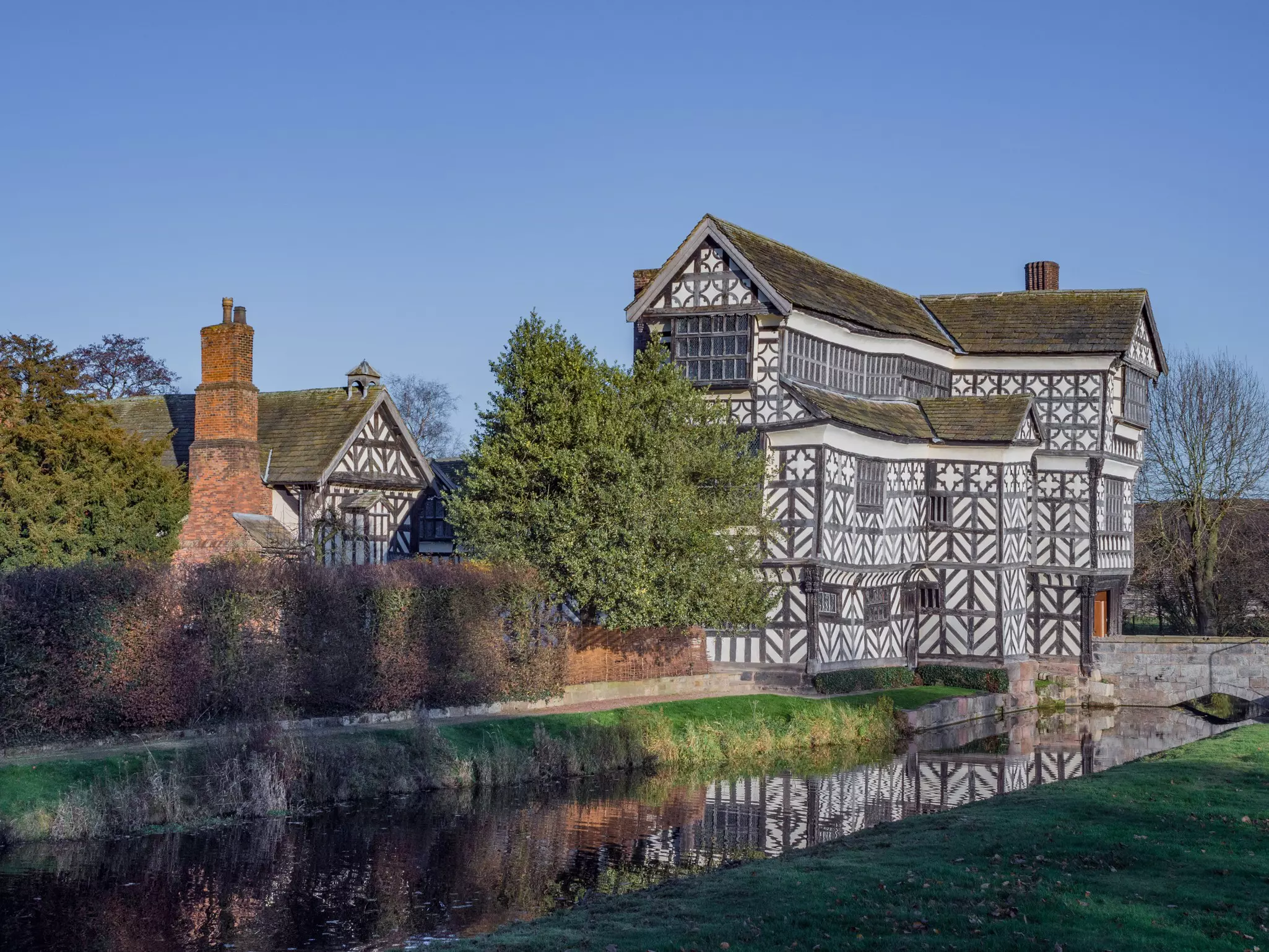 A tall timbered house, with a distinctive black and white facade, beside a moat