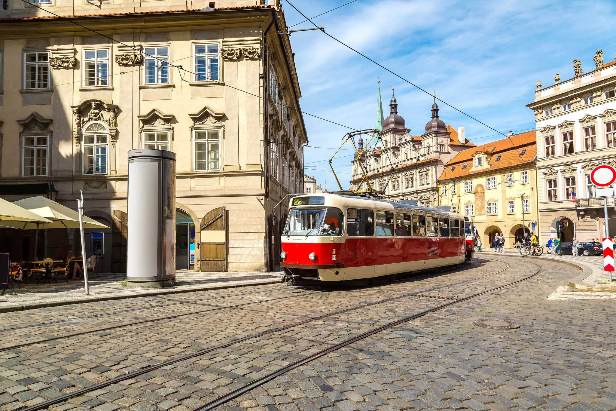A vintage-style tram runs along a cobbled street in Prague on a sunny summer day, Czechia.