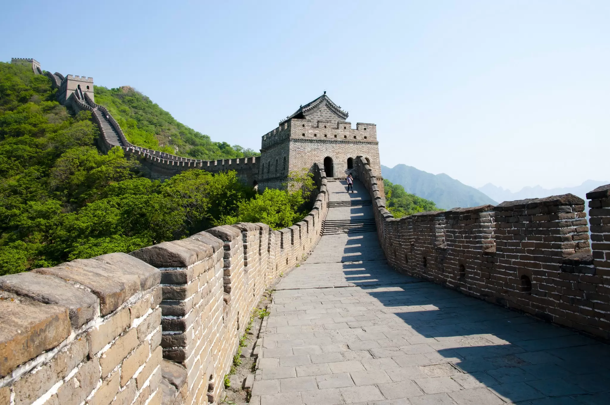 View of the Mutianyu section of the Great Wall of China, surrounded by greenery on a sunny day.