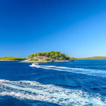 Speedboats leaving white wakes on deep blue sea beside small pine-covered Pakleni islets under a clear sky.