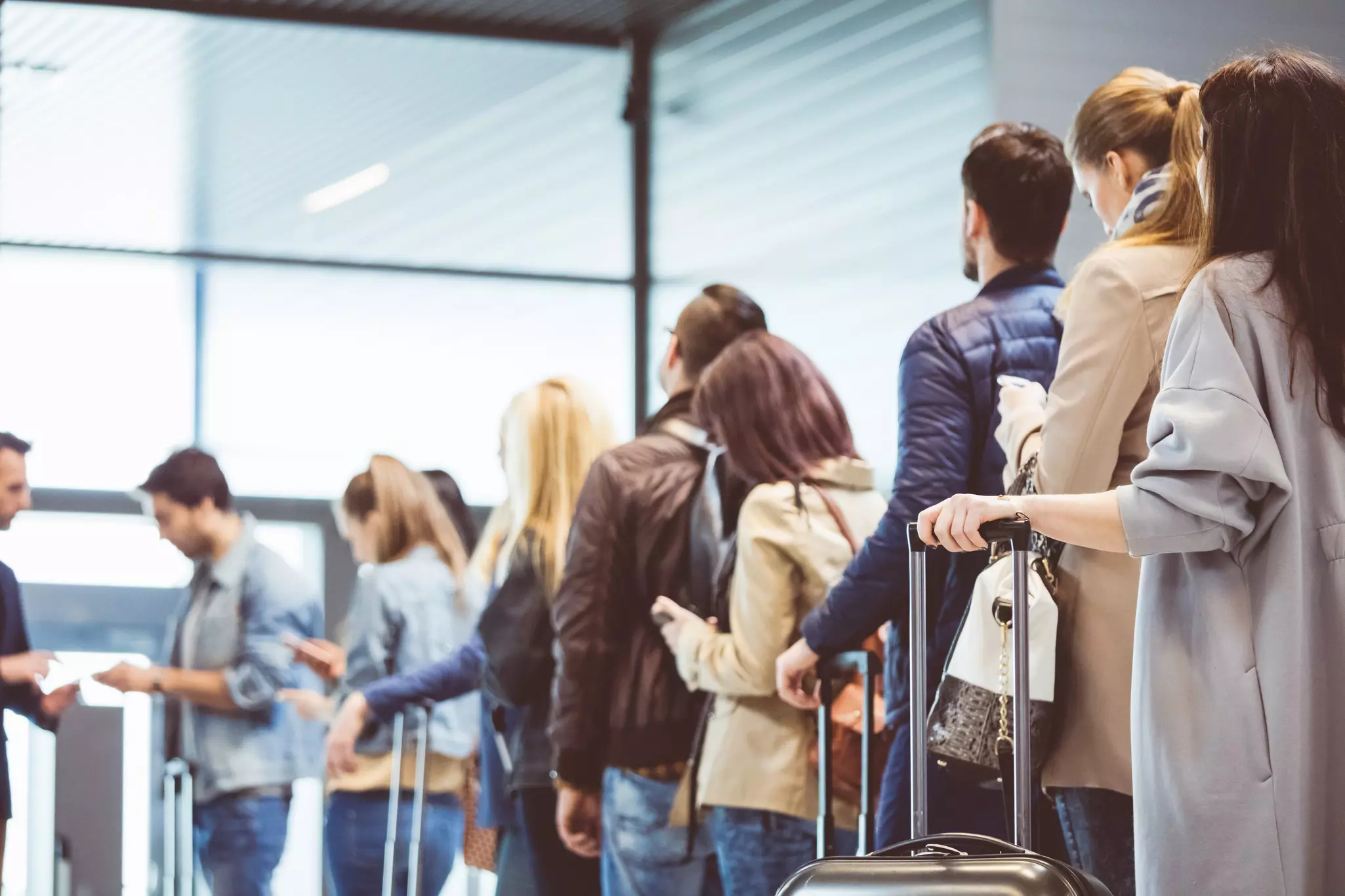 Crowds of people stand in an airport waiting.