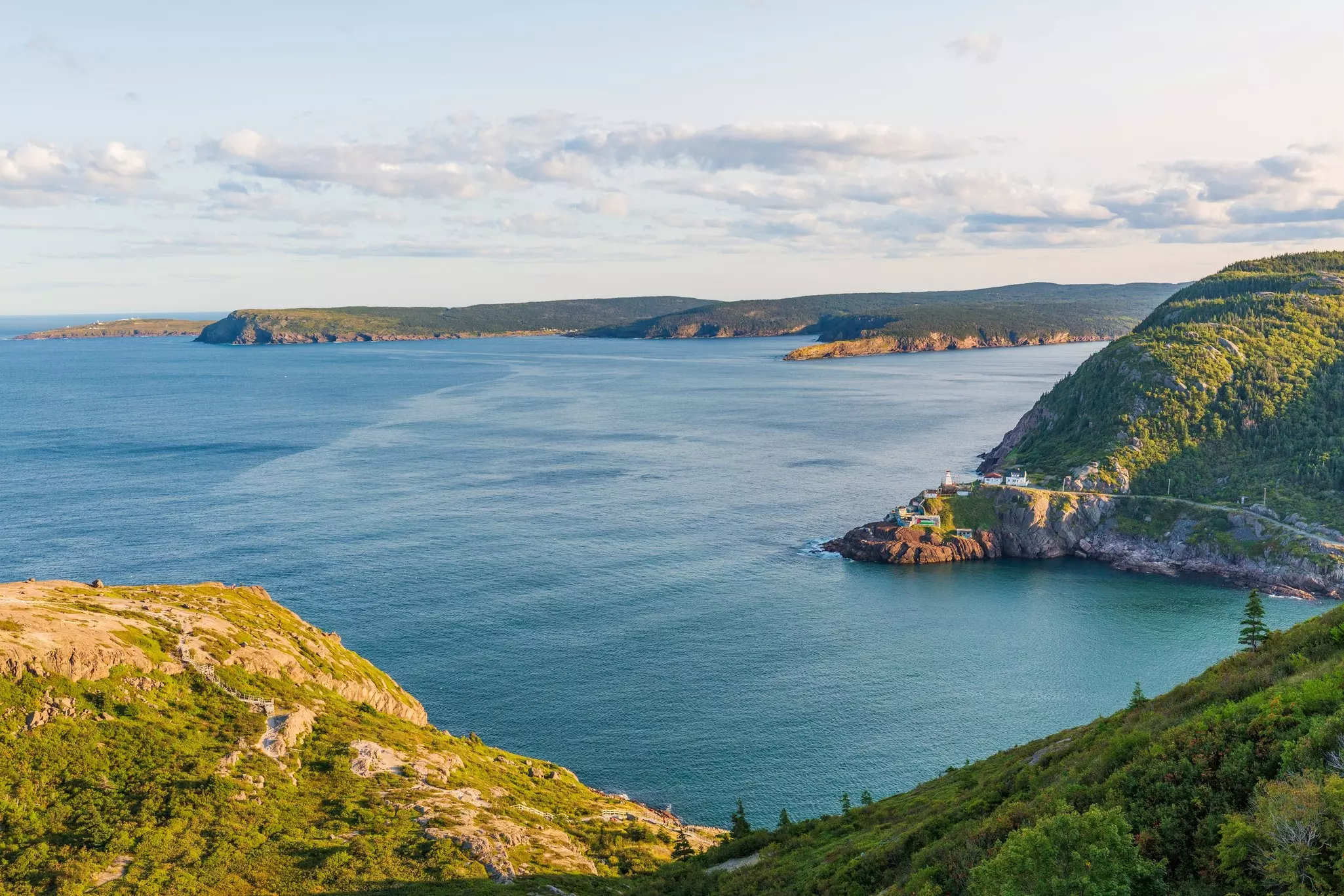 Aerial view of brush-covered rocky hills with the ocean in the distance on a mostly sunny day.