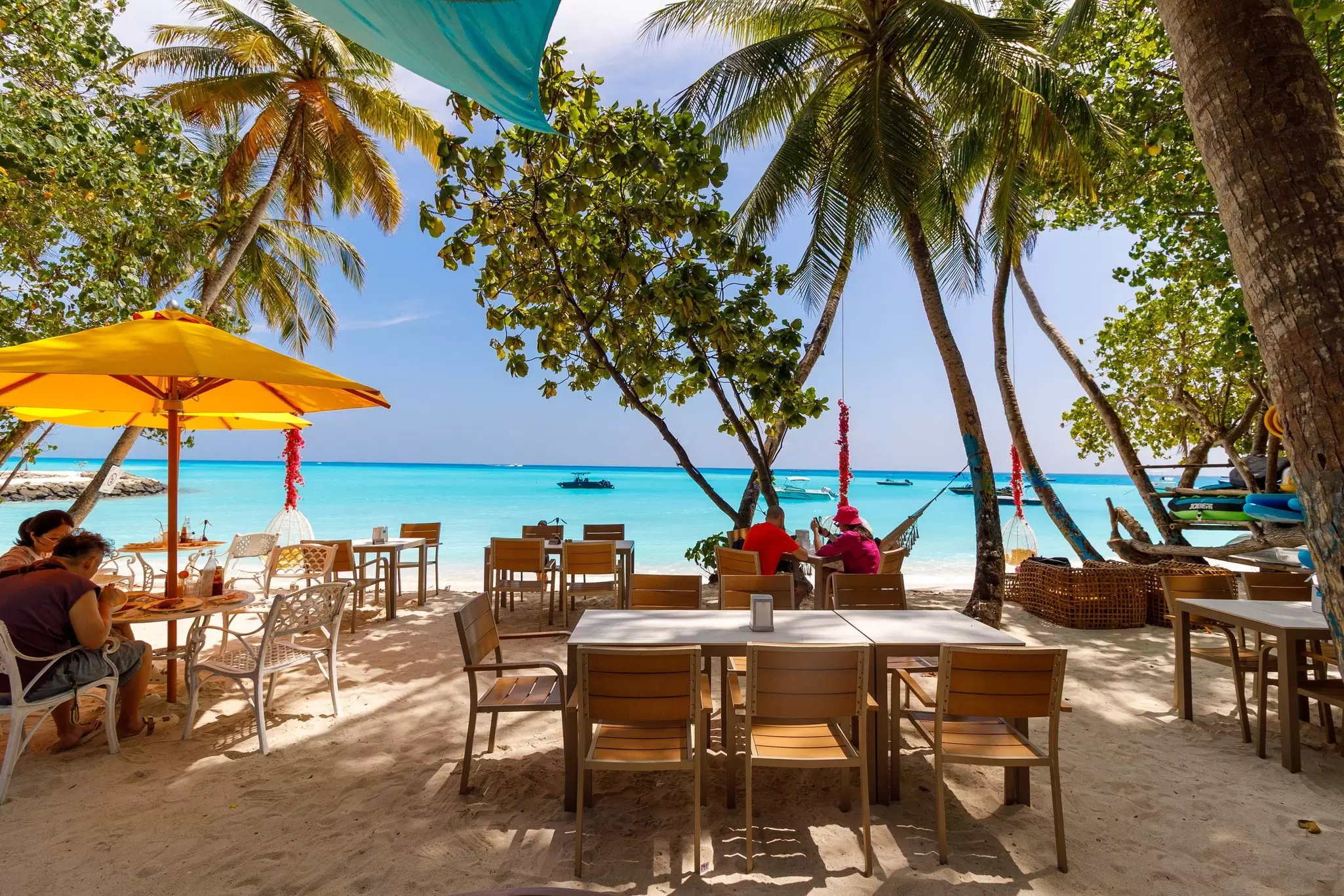 Diners sit at tables in the shade of palm trees just off the beach in Fulidhoo, Maldives