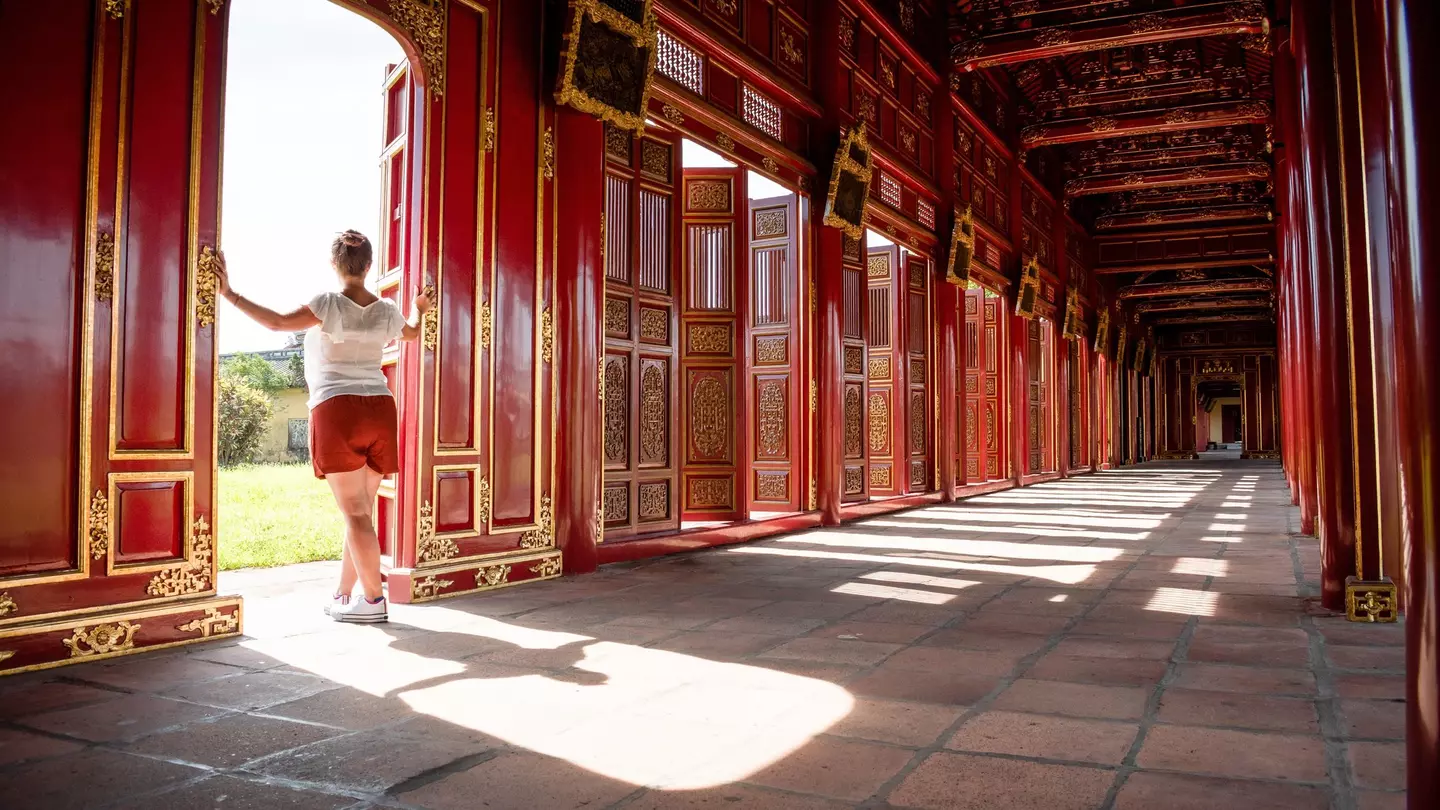 A tourist gazes out of the red and gold gates of the Imperial City of Hue, Vietnam.