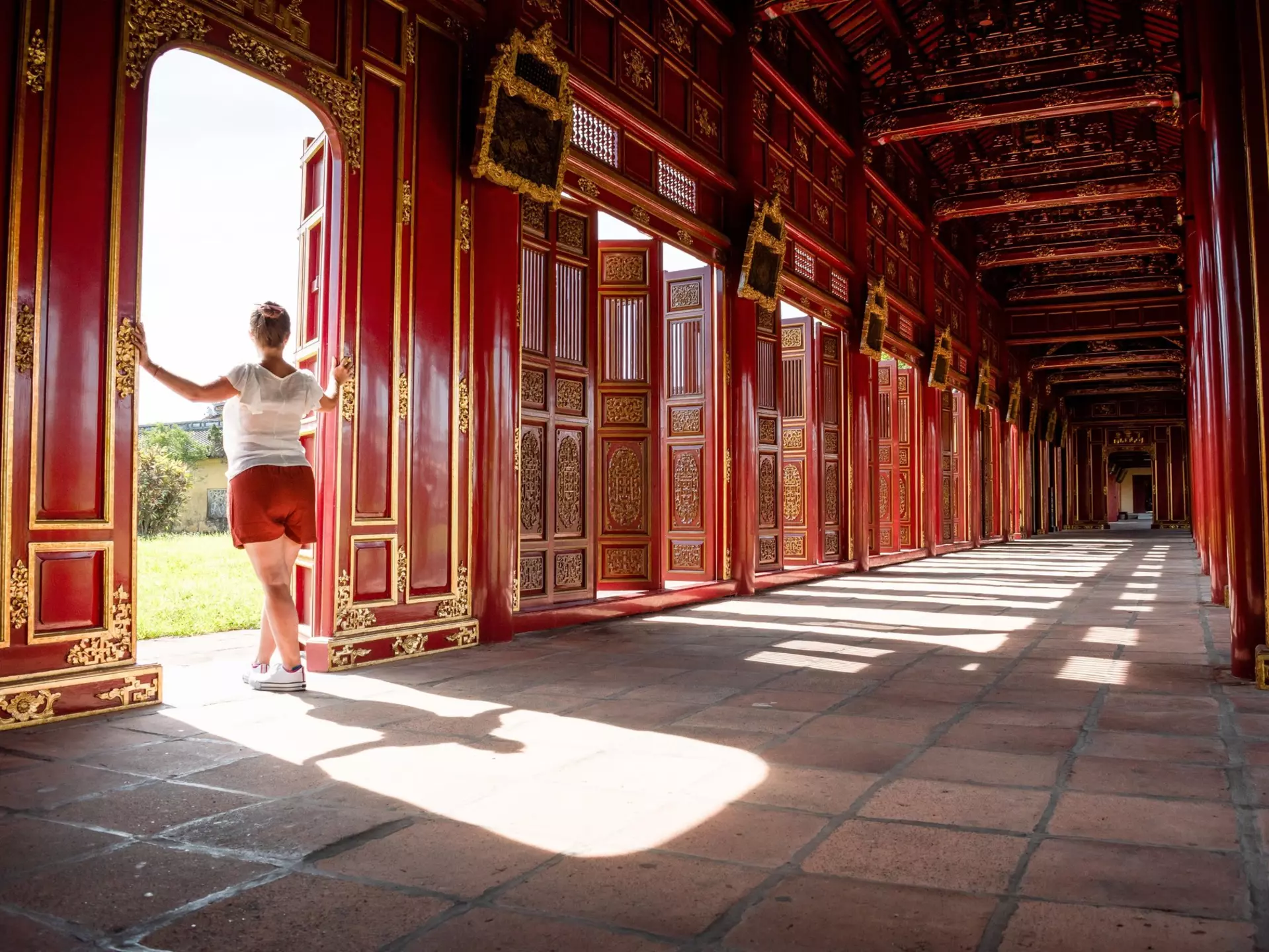 A tourist gazes out of the red and gold gates of the Imperial City of Hue, Vietnam.