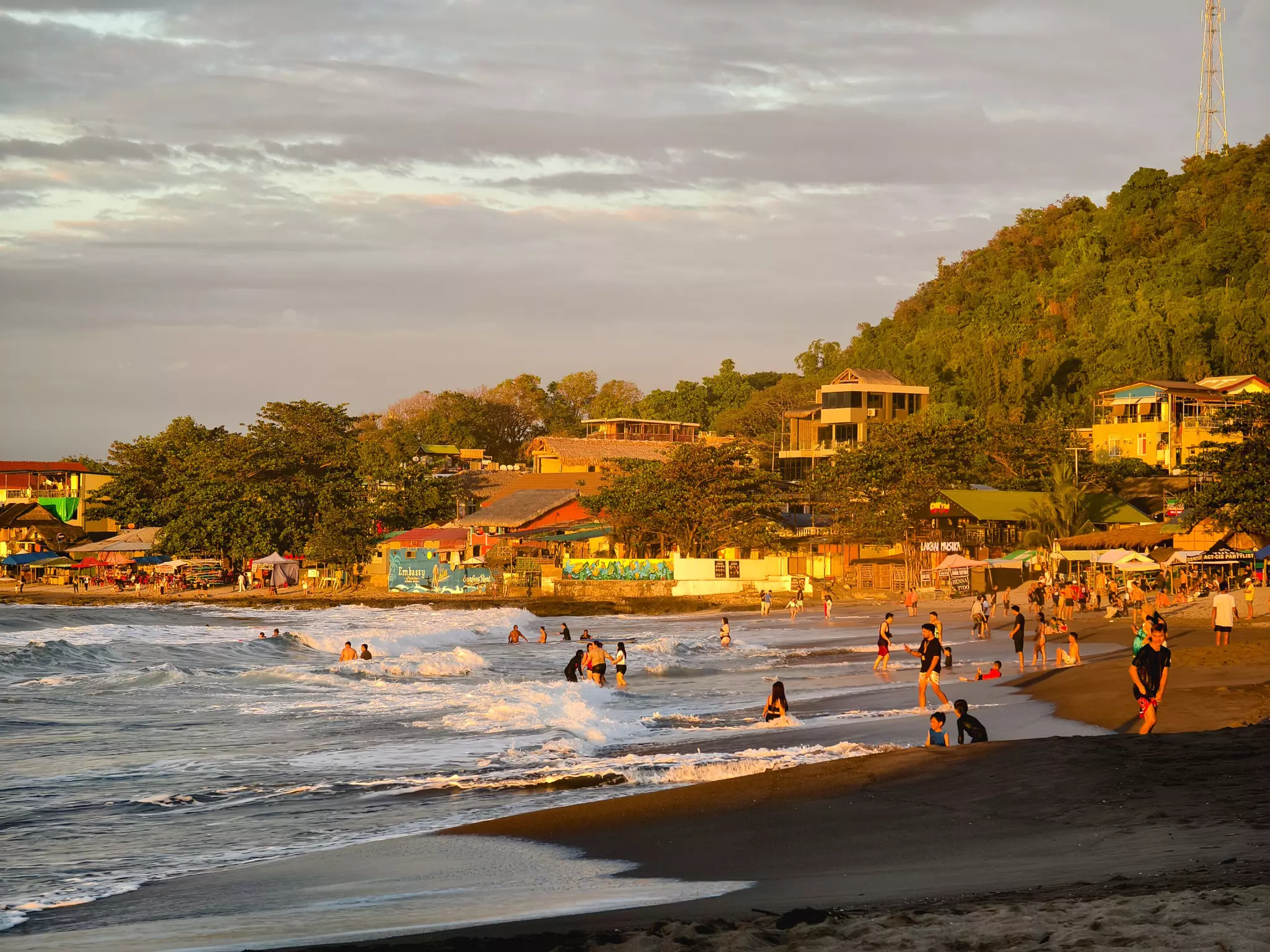 Swimmers in the ocean as the setting sun reflects off the low-rise beach-side restaurants.