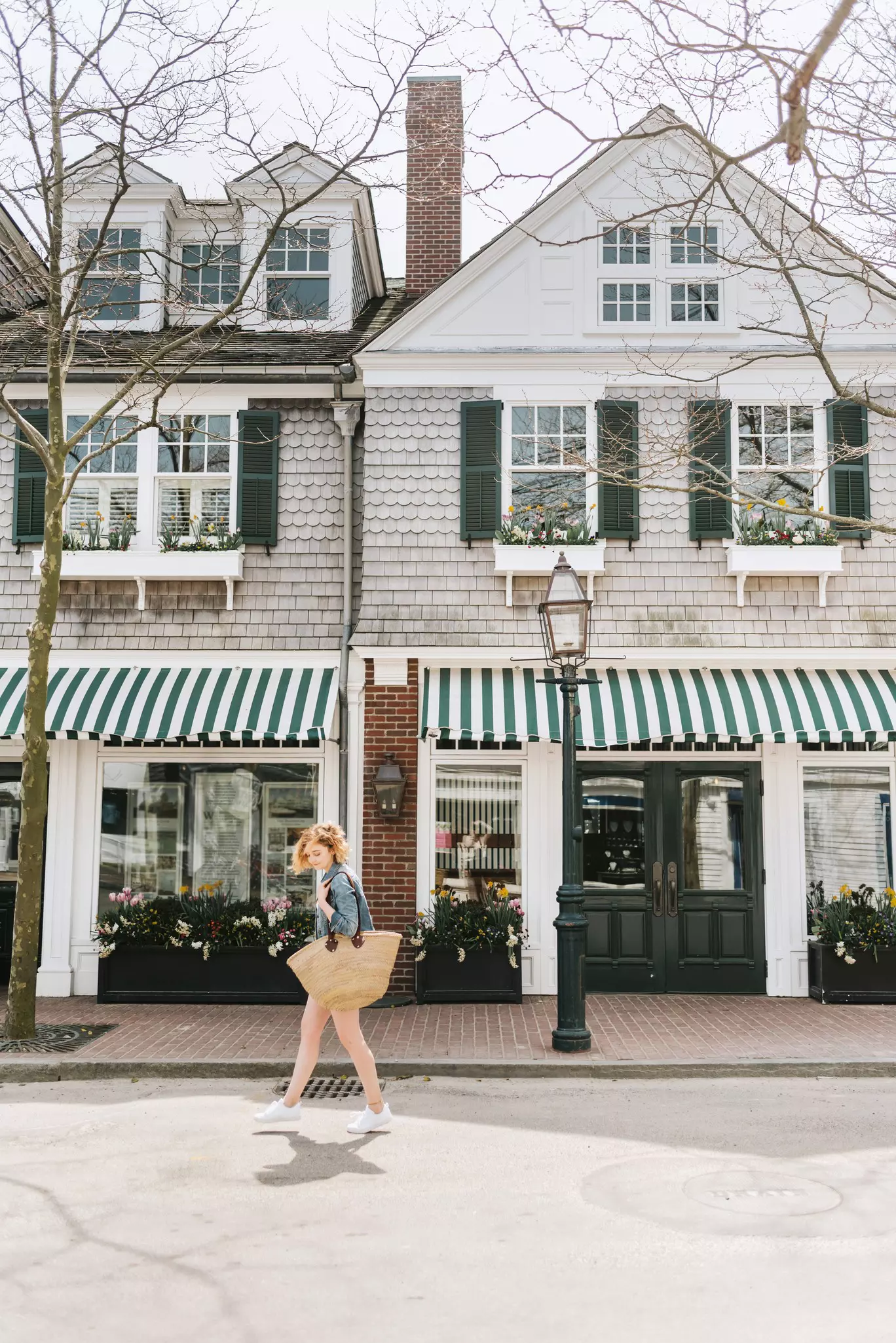 A woman carrying a large straw bag walks past a store with a striped green and white awning in Martha's Vineyard.