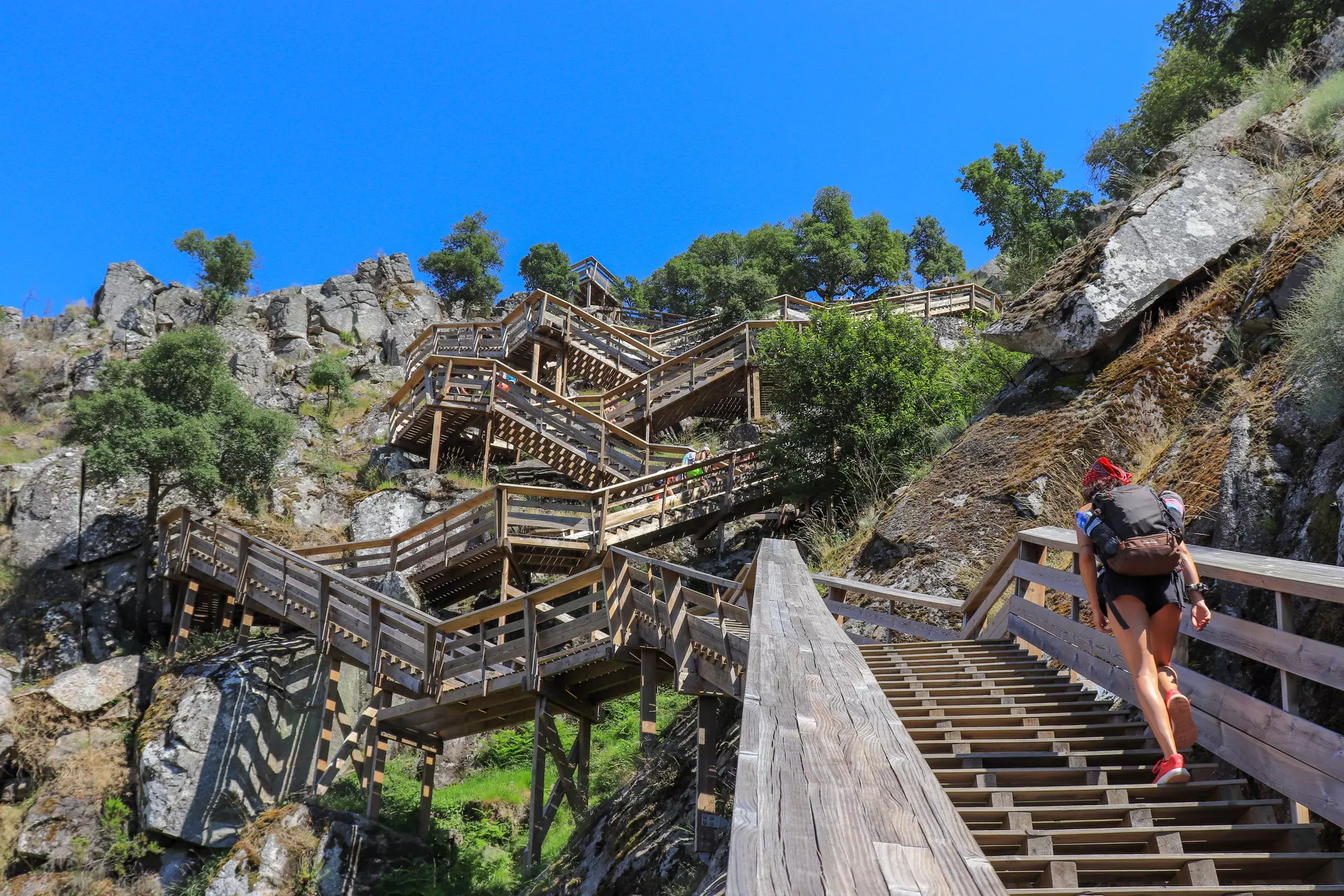 A person walking up a wooden staircase that crisscrosses a steep cliff.