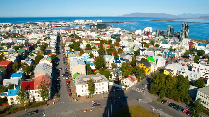An aerial view of Reykjavík, with the shadow of the Hallgrímskirkja falling over the colorful buildings of the city.