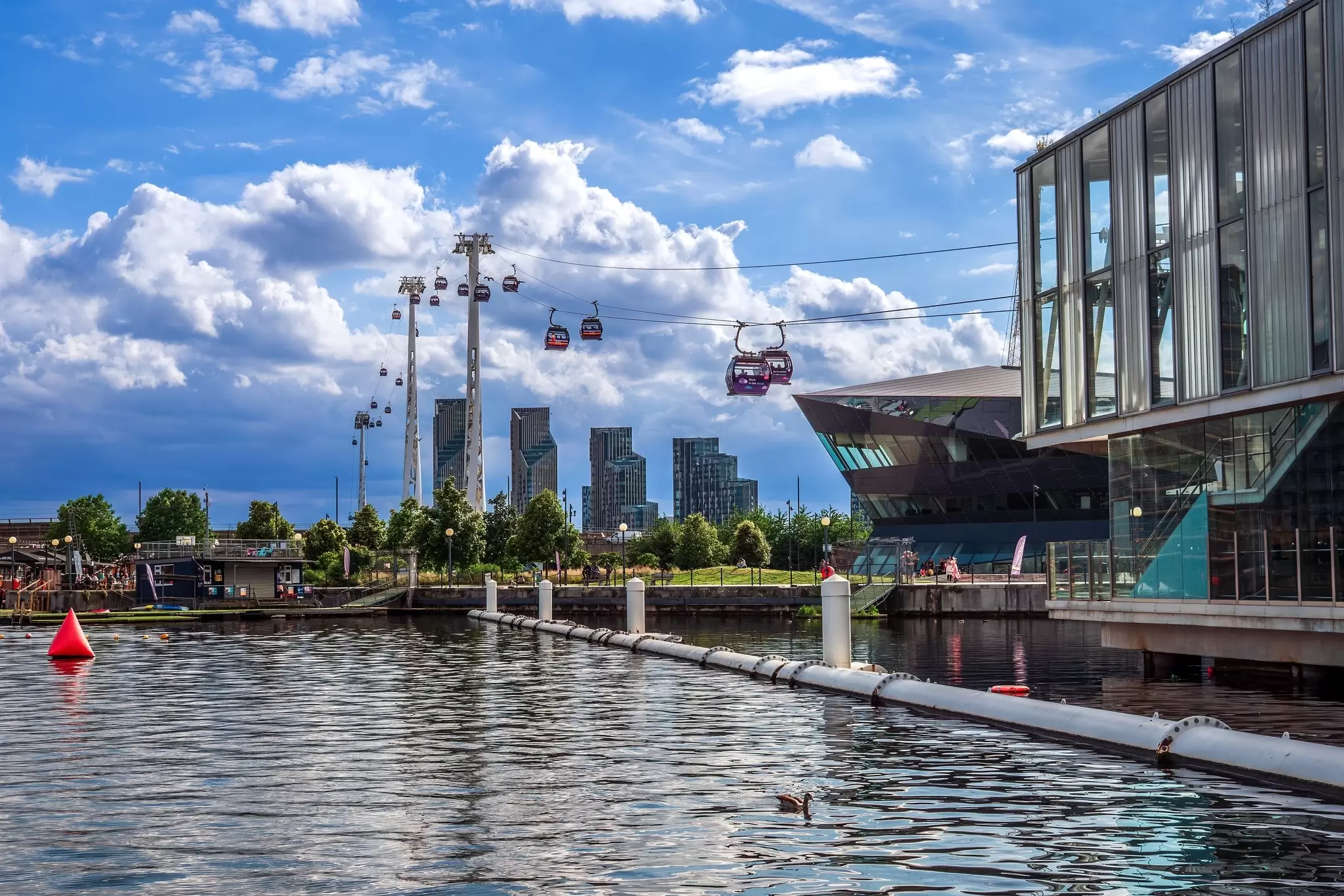 A series of cable car gondolas make their way over a dock and over a river: London Cable Car over Royal Victoria Dock. 