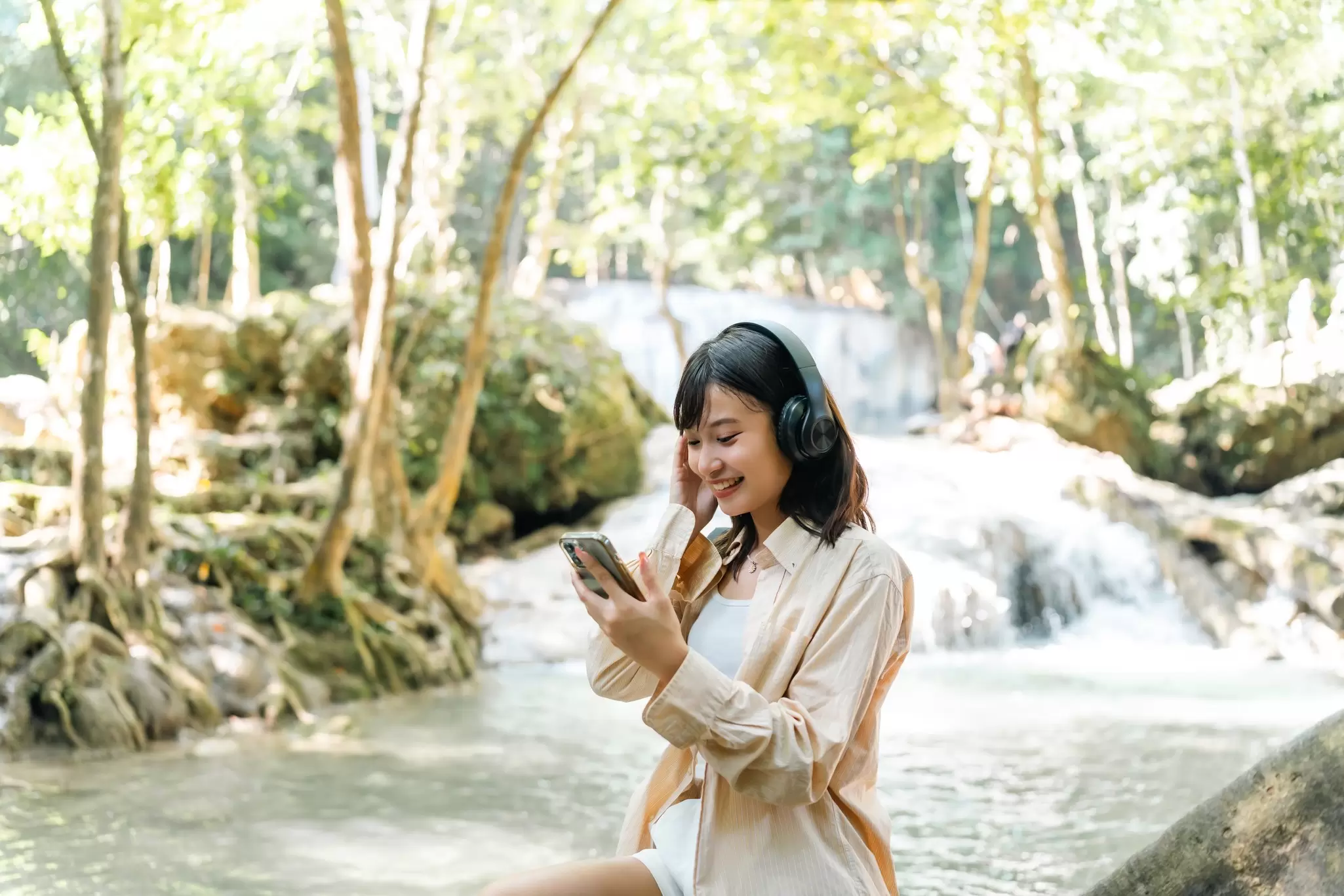 Young Asian woman listening to the music on headphones and mobile phone while travel nature hiking in forest on summer holiday vacation. People enjoy outdoor lifestyle relaxing by nature and waterfall, License Type: media, Download Time: 2025-10-21T13:53:29.000Z, User: rhylton_redventures, Editorial: false, purchase_order: 65050 - Digital Destinations and Articles, job: Lonely Planet, client: wip, other: Rhianydd Hylton