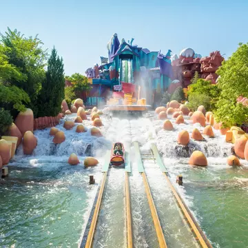 Water sprays around people riding down a log flume at a Florida theme park on a sunny day.