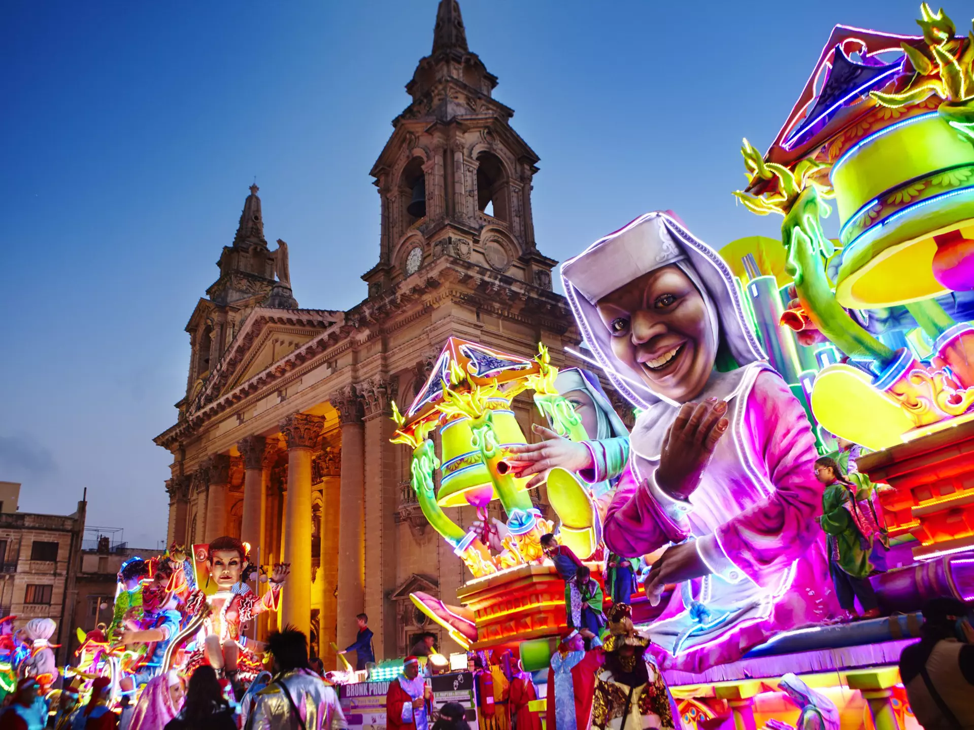 A neon-bright float inspired by the movie Sister Act passes by St Publius Parish Church in Floriana
