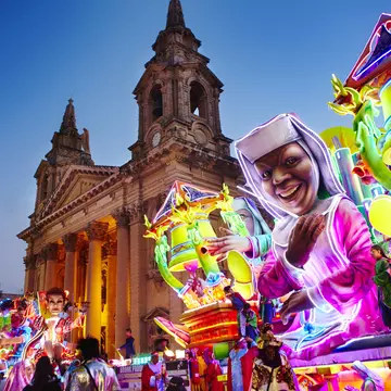 A neon-bright float inspired by the movie Sister Act passes by St Publius Parish Church in Floriana