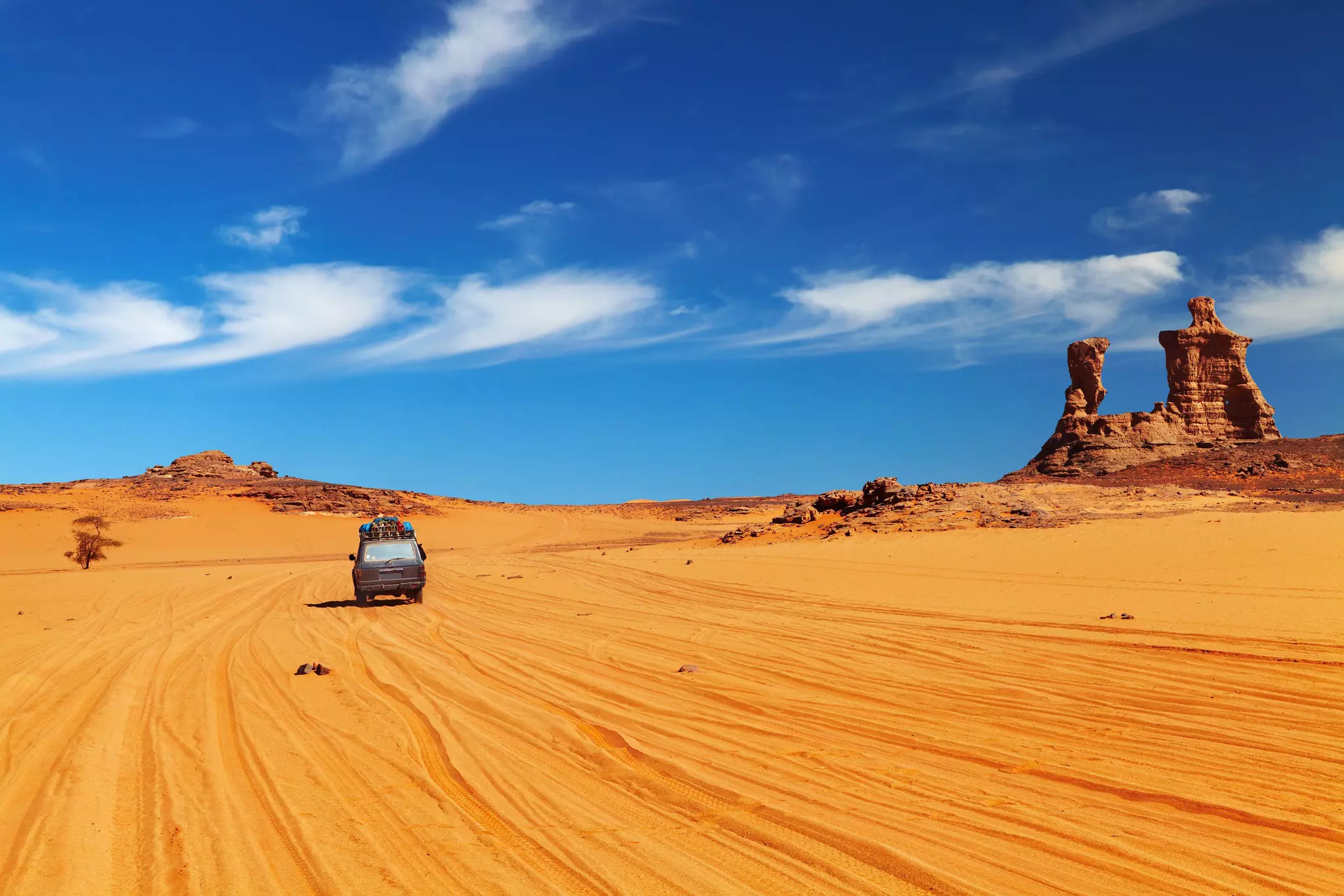 A four-wheel-drive truck on a sandy track through a desert landscape dotted with tall rock formations.