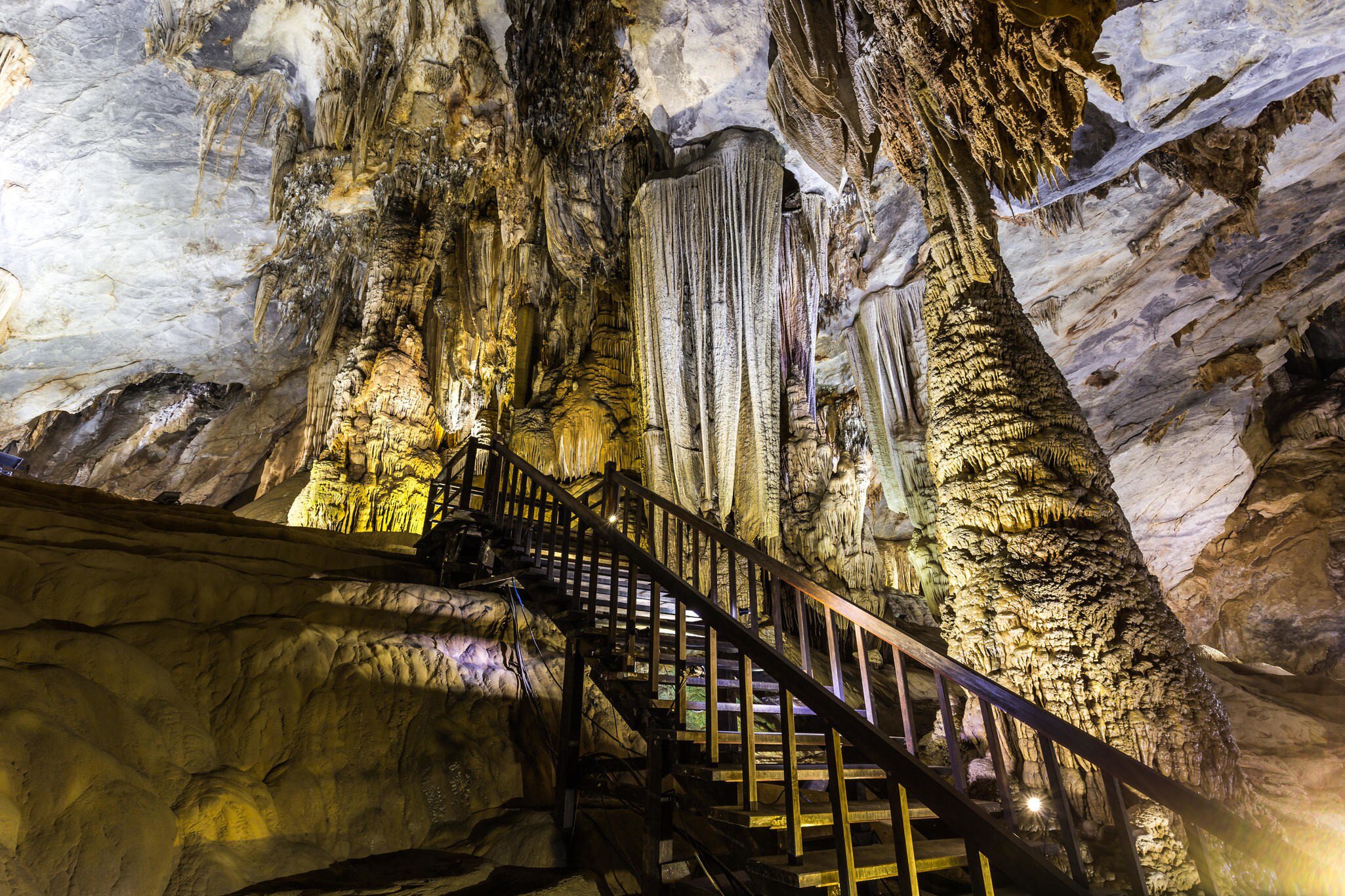 A wooden walkway descending among lit stalactites inside a cave.