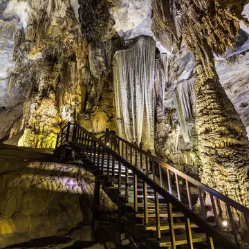 A wooden walkway descending among lit stalactites inside a cave.