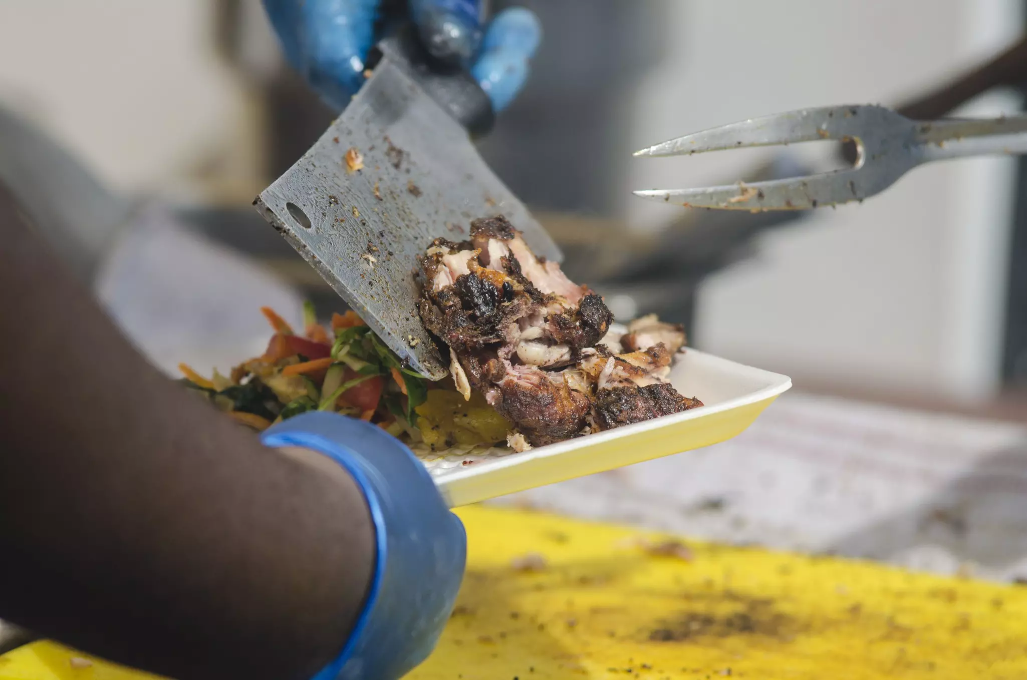A chef uses a butcher knife to pile a plate high with grilled jerk chicken