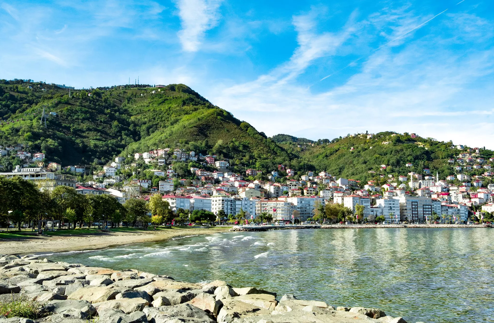 White buildings are clustered against a shoreline with a small beach, and a few buildings are set in the green hills behind.