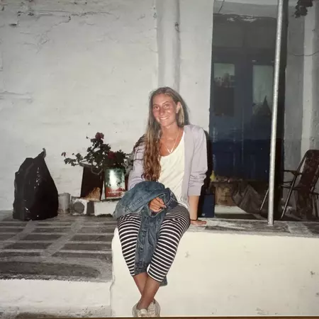 Caroline sitting on a white wall outside a house in Greece