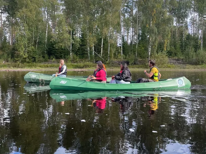 Four people canoeing in the forest while riding a green canoe
