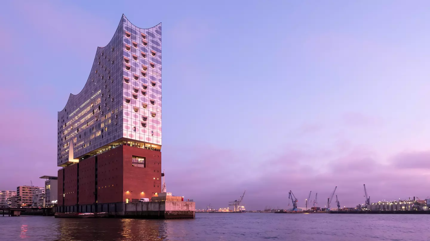 The Elbphilharmonie, viewed from the river, at dusk. A pink ligh is reflecting on the building's mirrored surface