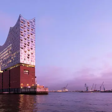 The Elbphilharmonie, viewed from the river, at dusk. A pink ligh is reflecting on the building's mirrored surface