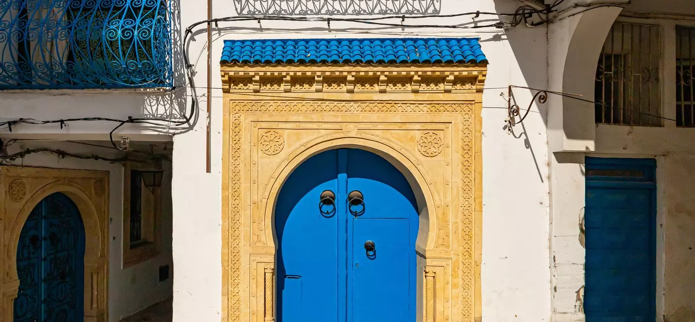A blue door decorated with knockers and framed by ochre-colored stone.